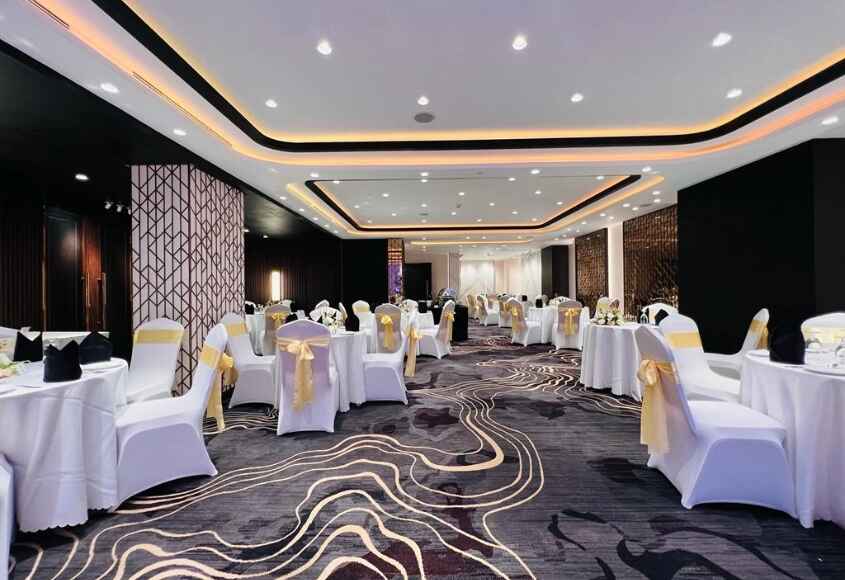 Elegant banquet hall with white chair covers, yellow sashes, decorated tables, and modern lighting.